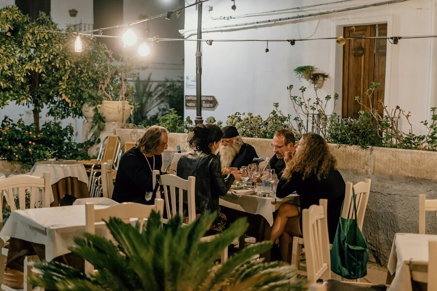 A group of friends sitting in an outdoor dining area with hanging lighting overhead.