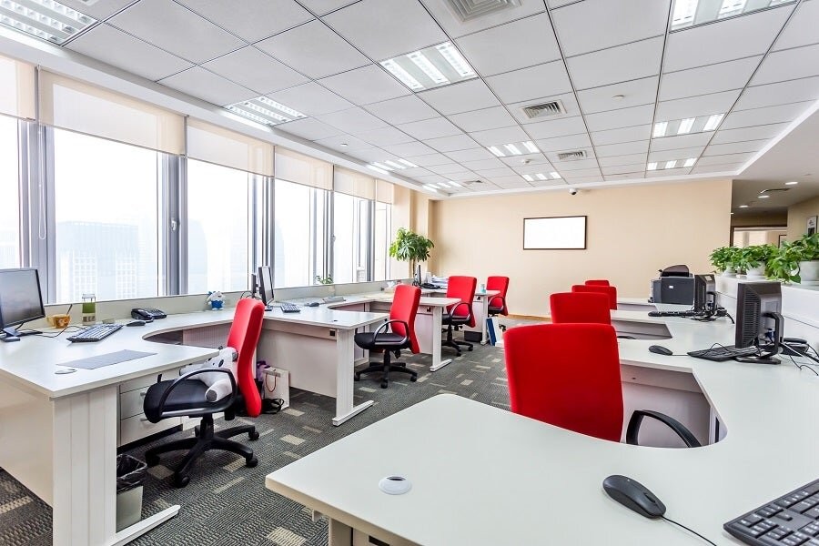 An office space with several desks and chairs with a large window featuring raised-up motorized shades in the background.