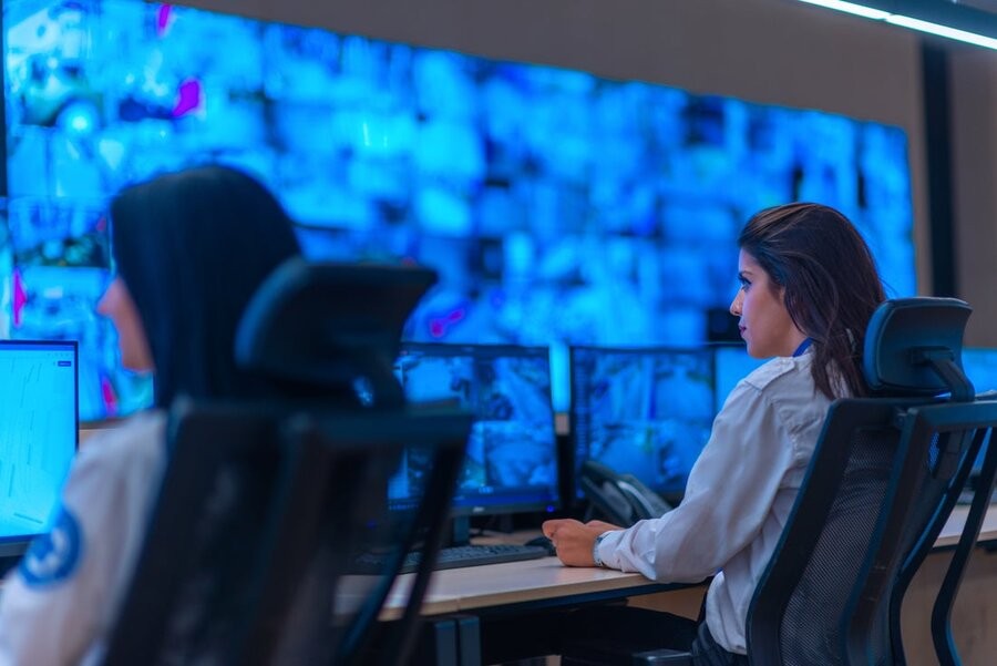 Two co-workers at their desks and screens in a control room of some type.