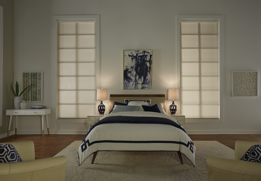 A dimly lit bedroom with two bedside lamps and two lowered motorized shades.